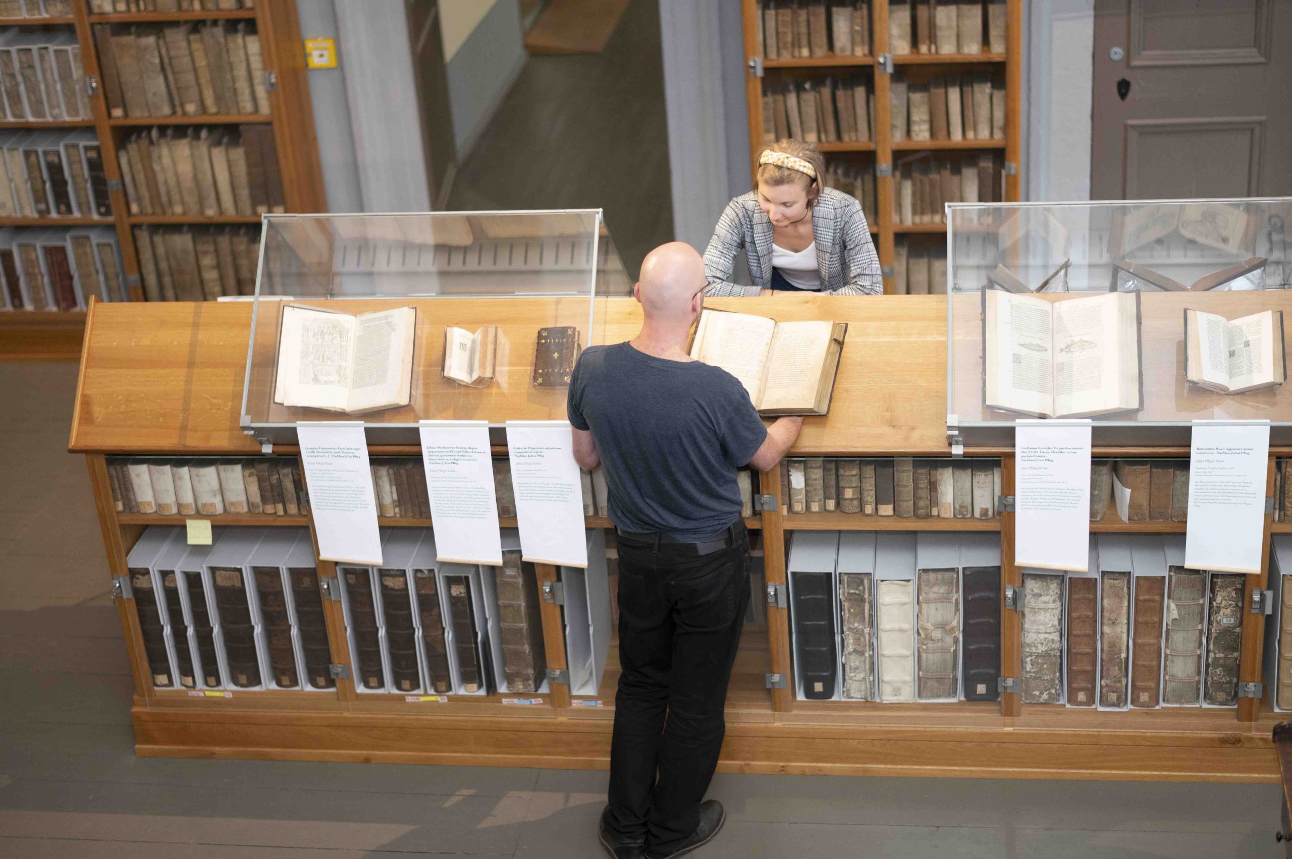 Ein Mann und eine Frau stehen vor aufgeschlagenen historischen Büchern