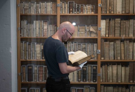 Mann vor Bücherregalen hält altes Buch mit Handschuhen fest