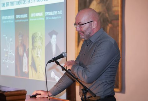 Matthias Ludwig am Mikrofon, im Hintergrund eine Präsentation